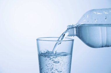 Pouring soda water from bottle into glass on light blue background, closeup. Space for text