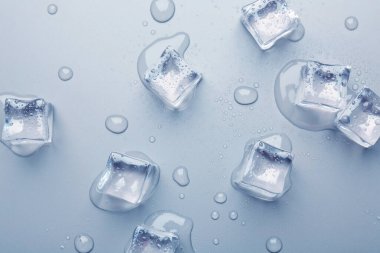 Eriyen buz küpleri ve açık mavi arkaplanda su damlaları, düz bir zemin