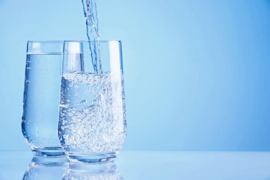 Açık mavi arkaplandaki bardaklara taze soda dökülüyor, yakın plan. Metin için boşluk