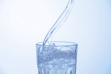 Açık mavi arkaplanda bardağa soda dökülüyor, yakın plan.