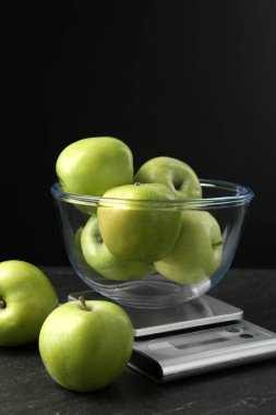 Elektronik mutfak terazisi, siyah arka planda koyu dokulu yeşil elma kasesi, yakın plan.