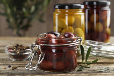 Cam kavanozlarda turşulu zeytin ve ahşap masada baharatlar, yakın plan.