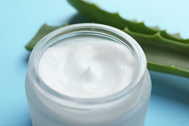 Açık mavi arkaplanda krema ve aloe yaprakları, yakın plan