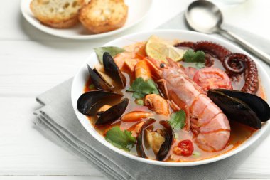 Beyaz ahşap masada servis edilen lezzetli deniz ürünleri çorbası, yakın plan.