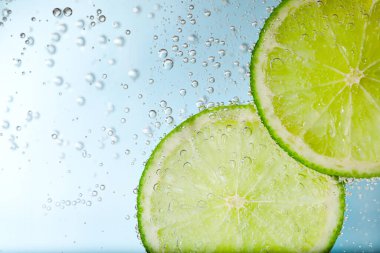 Açık mavi arka planda limon dilimli soda, yakın plan.