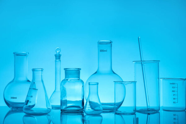 Laboratory glassware on mirror surface against light blue background