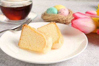 Lezzetli kek parçaları, Paskalya yumurtaları, laleler ve çay gri masada, yakın plan.