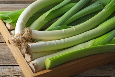 Fresh leeks in crate on wooden table, closeup