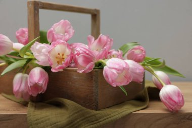 Güzel laleler sepetin içinde ahşap masada, gri arka planda, yakın planda.
