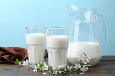 Taze süt ve çiçekler beyaz masada açık mavi arka planda