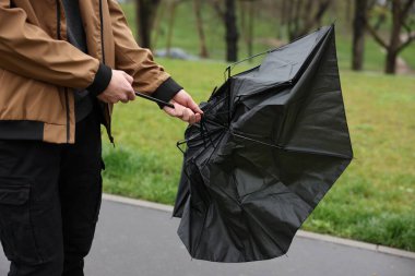 Kırık şemsiyeli bir adam yağmur altında rüzgarla savaşıyor.