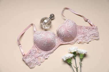 Pembe dantelli sutyen, parfüm ve çiçekli bej arka plan, düz yatış
