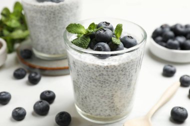 Delicious chia pudding with blueberries and mint in glasses on white table, closeup