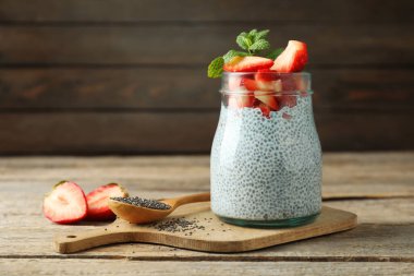 Çilekli lezzetli chia pudingi ve ahşap masada cam kavanozda nane şekeri.