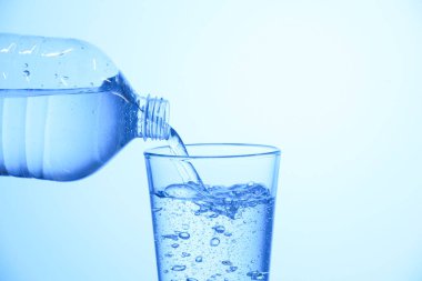 Pouring soda water from bottle into glass on light blue background, closeup. Space for text