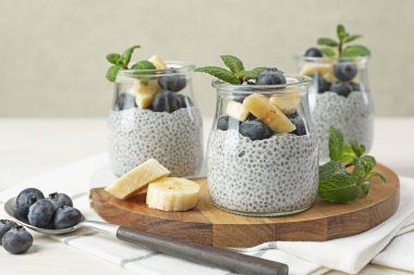 Yaban mersinli lezzetli chia pudingi, muzlu ve naneli bardaklar ışıklı masada, yakın plan.