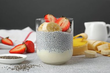 Çilekli lezzetli chia pudingi ve açık gri masada cam içinde muz.