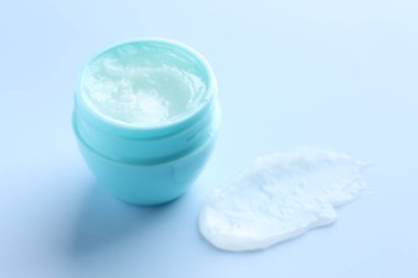 Açık mavi arkaplanda nemlendirici dudak kremi ve kavanoz, yakın plan.