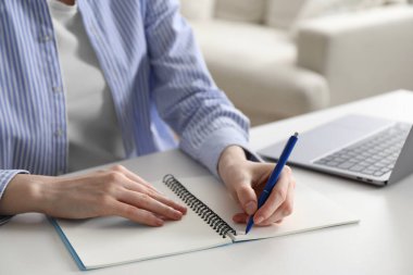 Beyaz masa içerisindeki çevrimiçi derste not alan bir kadın, yakın plan. Kendi kendine çalışma.