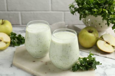Sağlıklı maydanoz bardakta içer, yapraklar ve elmalar beyaz mermer masada, yakın plan