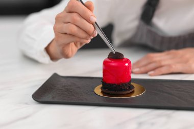 Şekerci lezzetli bir tatlıyı masada bir parça çikolatayla süslüyor, yakın plan.