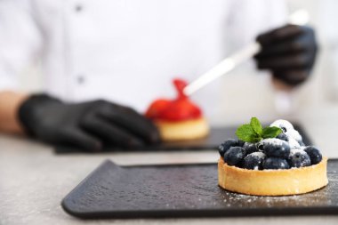 Mutfaktaki gri masada çilekli lezzetli tart süsleyen şekerci, tatlıya odaklan.