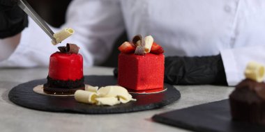 Mutfaktaki açık gri masada lezzetli bir tatlıyı dekore eden şekerci, yakın plan.