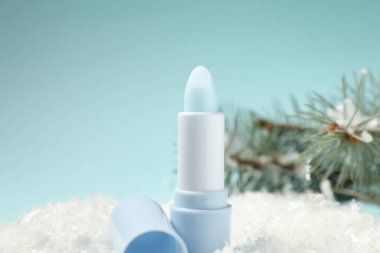 Nemlendirici dudak kremi ve yapay kar üzerindeki köknar ağacı dalları açık mavi arka planda, yakın plan. Kış bakımı