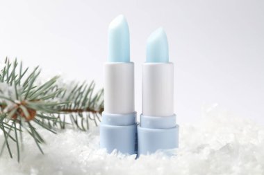 Nemlendirici dudak kremleri ve suni kar üzerindeki köknar ağacı dalları beyaz arka planda, yakın plan. Kış bakımı