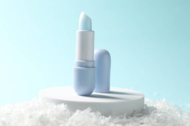 Yapay kar üzerindeki nemlendirici dudak kremi açık mavi arka planda, yakın plan. Kış bakımı