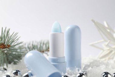 Nemlendirici dudak kremleri, Noel dekorasyonu ve beyaz arka planda suni kar üzerindeki köknar ağacı dalları, yakın plan. Kış bakımı