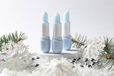 Nemlendirici dudak kremleri, Noel dekorasyonu ve beyaz arka planda suni kar üzerindeki köknar ağacı dalları, yakın plan. Kış bakımı