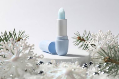 Nemlendirici dudak kremi, Noel dekorasyonu ve beyaz arka planda suni kar üzerindeki köknar ağacı dalları, yakın plan. Kış bakımı