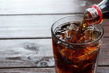Ahşap masada şişeden bardağa ferahlatıcı kola doldurmak, yakın plan. Metin için boşluk
