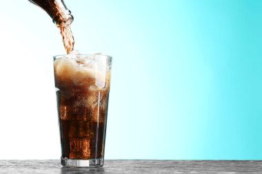 Karanlık desenli masada, turkuaz gradyan arka planda şişeden cama ferahlatıcı kola dökülüyor, yakın plan. Metin için boşluk