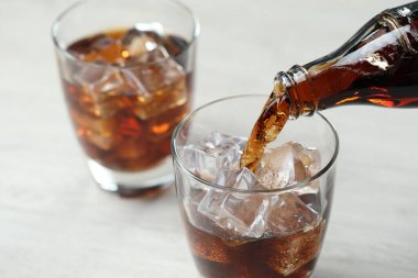 Açık gri masada şişeden bardağa ferahlatıcı kola dökülüyor, yakın plan.