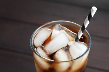 Kola buz küpleriyle tazeleniyor ve bulanık arkaplanda bardakta pipet, yakın plan