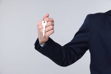 Emlakçı elinde ev şekilli anahtarlık açık gri arka planda, yakın plan.