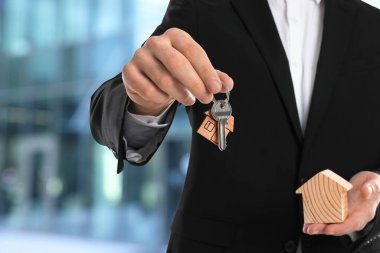 Emlakçının elinde anahtar ve ahşap ev modeli var.