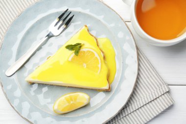 Beyaz ahşap masada servis edilen limon kaymaklı leziz peynirli kek.