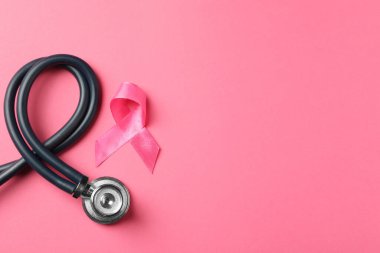 Göğüs kanseri farkındalığı. Renkli arka planda pembe kurdele ve steteskop, düz konum. Metin için boşluk