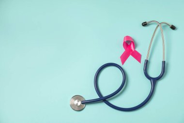 Göğüs kanseri farkındalığı. Açık mavi arka planda pembe kurdele ve steteskop. Metin için boşluk
