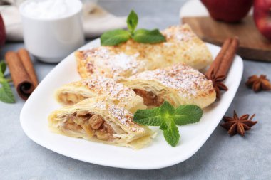 Açık gri masada pudra şekeri, nane ve baharatla lezzetli elmalı turtalar, yakın plan.