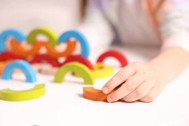 Motor beceri geliştirme. Beyaz masada renkli ahşap parçalarla oynayan küçük kız, yakın plan.