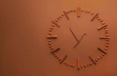 Tarçın çubukları, badem ve vanilya kabukları kahverengi zemin üzerindeki saati temsil ediyor. Metin için boşluk