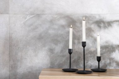 Kapalı alandaki gri mermer duvarın yanındaki ahşap masada yanan mumlarla süslü şamdanlar.