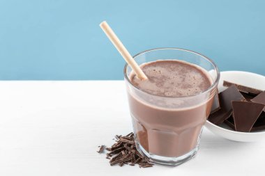 Lezzetli çikolatalı süt, beyaz masadaki talaş ve parçalarla açık mavi arka plan, yakın plan. Metin için boşluk