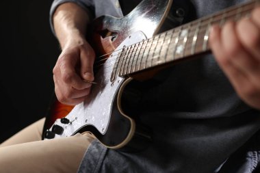 Siyah arkaplanda arabulucuyla gitar çalan adam, yakın plan