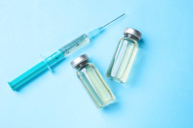 Cam şişelerde Hepatit aşısı ve açık mavi arka planda şırınga.