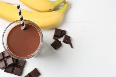 Bardakta çikolatalı süt, beyaz masada parçalar ve muzlar, düz yatak. Metin için boşluk